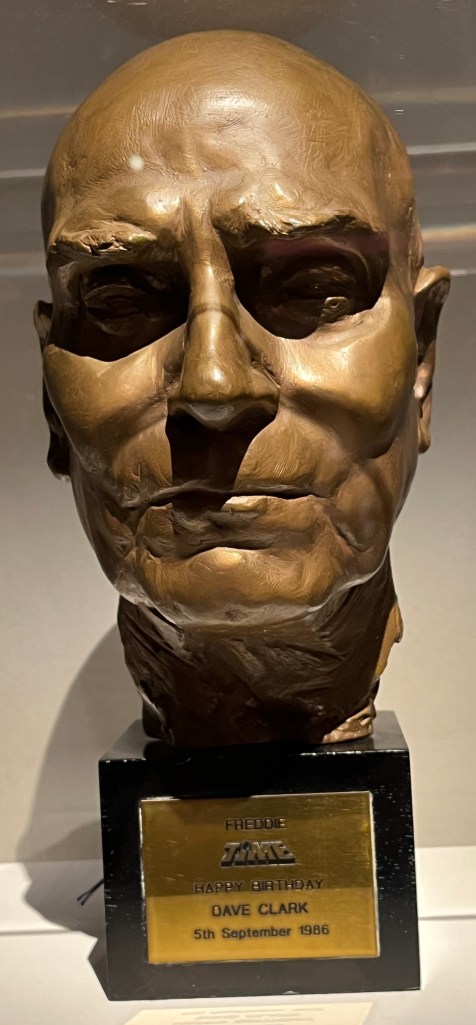 A bronze bust of Sir Laurence Olivier's head. A gold plaque on the base has black text that reads Freddie, Time, Happy Birthday, Dave Clark, 5th September 1986
