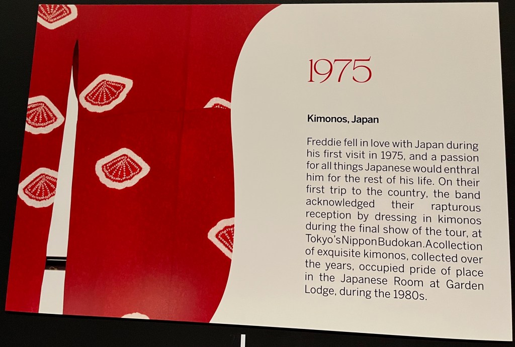 A white board on the Freddie Mercury timeline in Sotheby's. Alongside a close-up of white seashells on a red kimono is text that reads 1975 - Kimonos, Japan. Freddie fell in love with Japan during his first visit in 1975, and a passion for all things Japanese would enthral him for the rest of his life. On their first trip to the country, the band acknowledged their rapturous reception by dressing in kimonos during the final show of the tour, at Tokyo's Nippon Budokan. A collection of exquisite kimonos, collected over the years, occupied pride of place in the Japanese Room at Garden Lodge, during the 1980s.