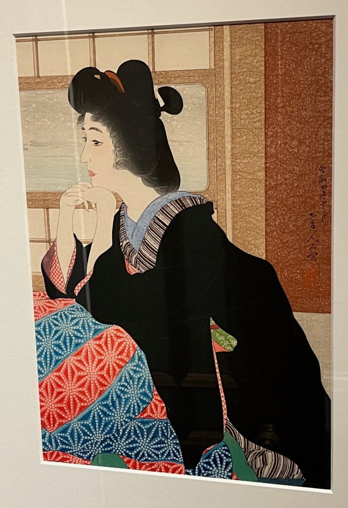 Woodblock print depicting a Japanese lady sitting on the floor, leaning her elbows on her bent-up knees and resting her chin on her interlocked hands. She looks thoughtful, while snow can be seen falling through the window behind her.