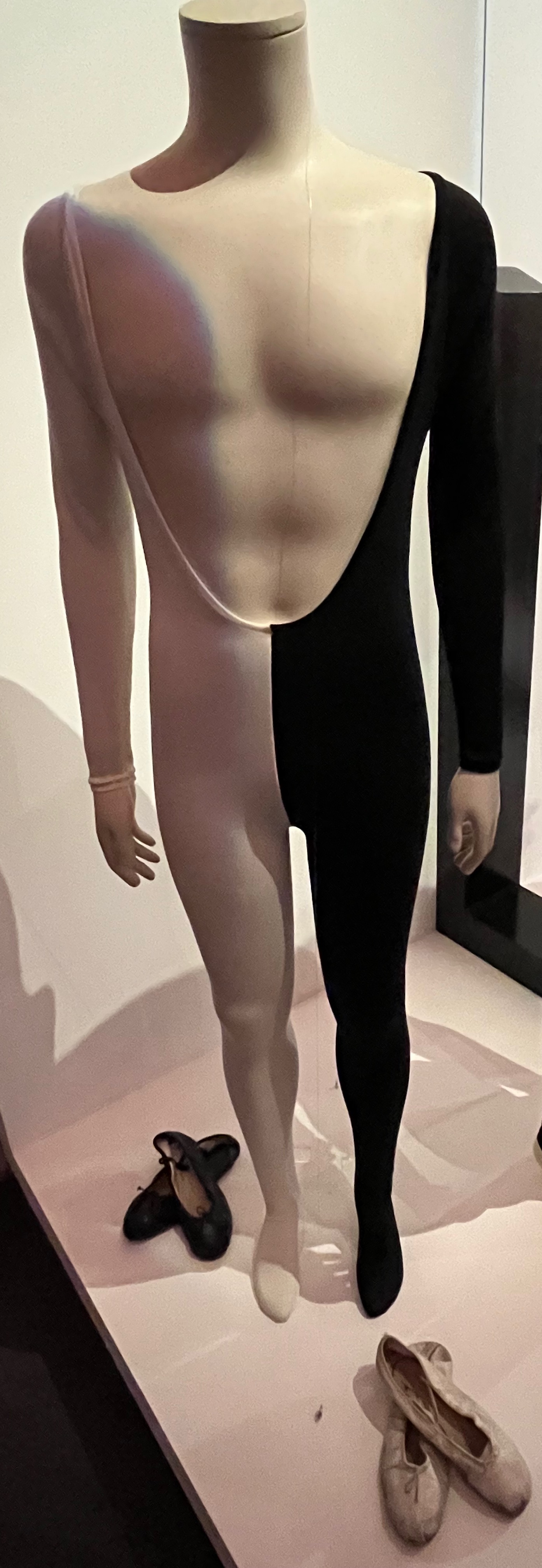 A half black and half white long-sleeved elastane catsuit with deep scooped neckline and integral feet, the right half white, the left half black.