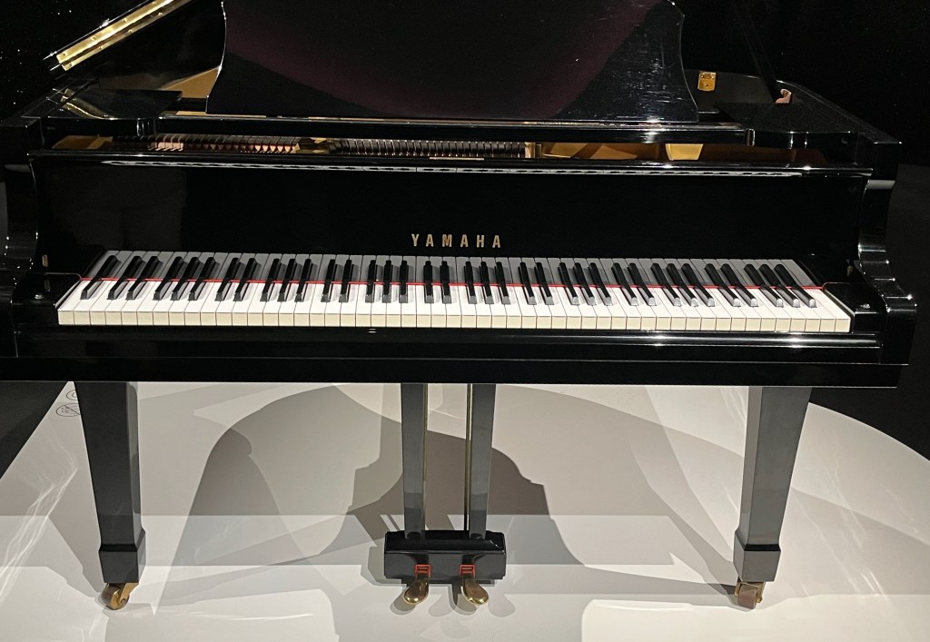 Front view of Freddie Mercury's black baby grand Yamaha piano, the keys reflected in the highly polished front surface.