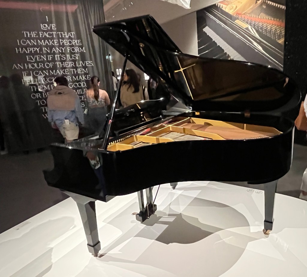 Rear view of Freddie Mercury's black baby grand Yamaha piano, the lid lifted fully open to reveal the strings inside.