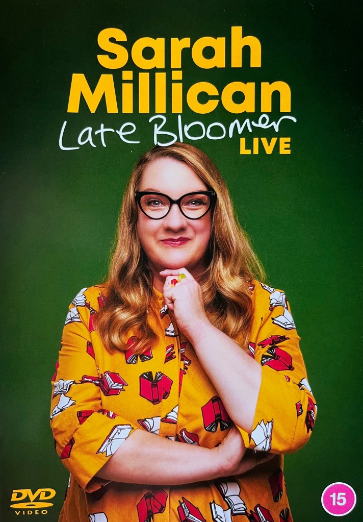The front cover of Sarah Millican's Late Bloomer DVD, showing the comedian smiling while wearing a light orange top covered in images of open books with red covers.