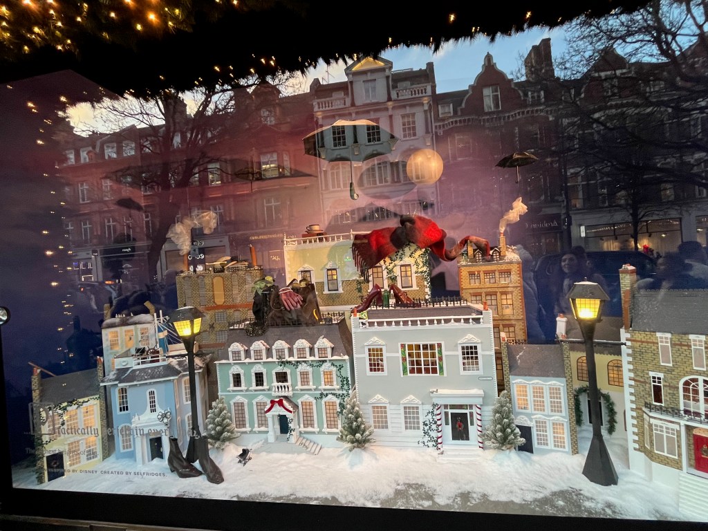 Selfridges window display representing Mary Poppins, showing a detailed model of a street in the snow, while a black umbrella floats high overhead.