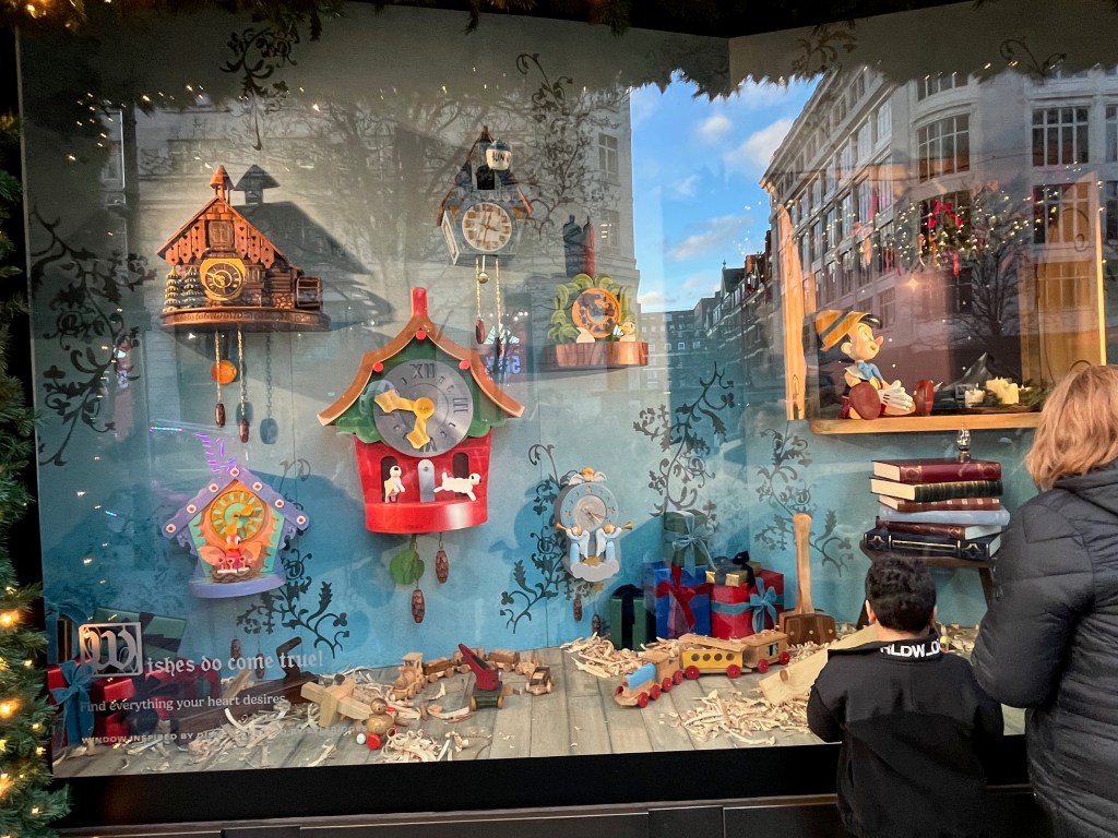 Selfridges window display representing Pinocchio, showing the workshop where he's created, with the puppet sitting on a shelf, while nearby are clocks with a variety of intricate designs.
