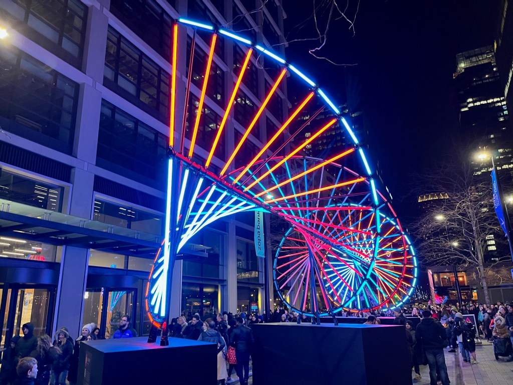 Blueprint, an artwork lit up in blue, yellow and red colours that looks like a double helix strand of DNA, with 2 spiralling lines linked by straight lines. The artwork is viewed from one end, so it appears to spiral off into the distance.