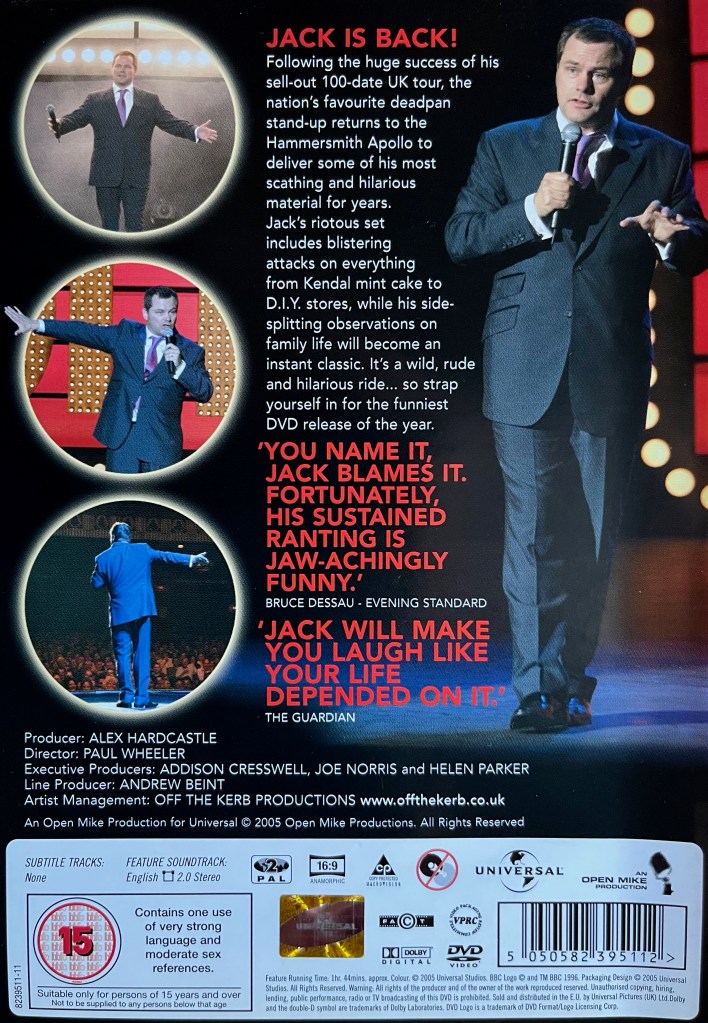 Back cover of the DVD for Jack Dee Live Again. The description and review quotes in the centre are flanked by 3 circular images of Jack performing on the left, and a full length photo of Jack on stage on the right, wearing a grey suit over a white shirt. Credits along with technical and copyright information are at the bottom of the cover.