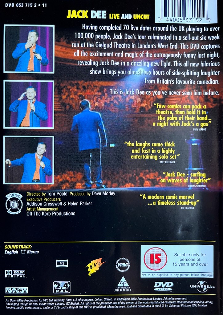 Back cover of the DVD for Jack Dee Live And Uncut. The main image, over which the description and review quotes are printed, shows a rear view of Jack performing on stage, looking out towards the audience. Down the left hand side are three square boxes showing a front view of Jack talking during the show. Technical and copyright information is then shown across the bottom in white text against the black background.