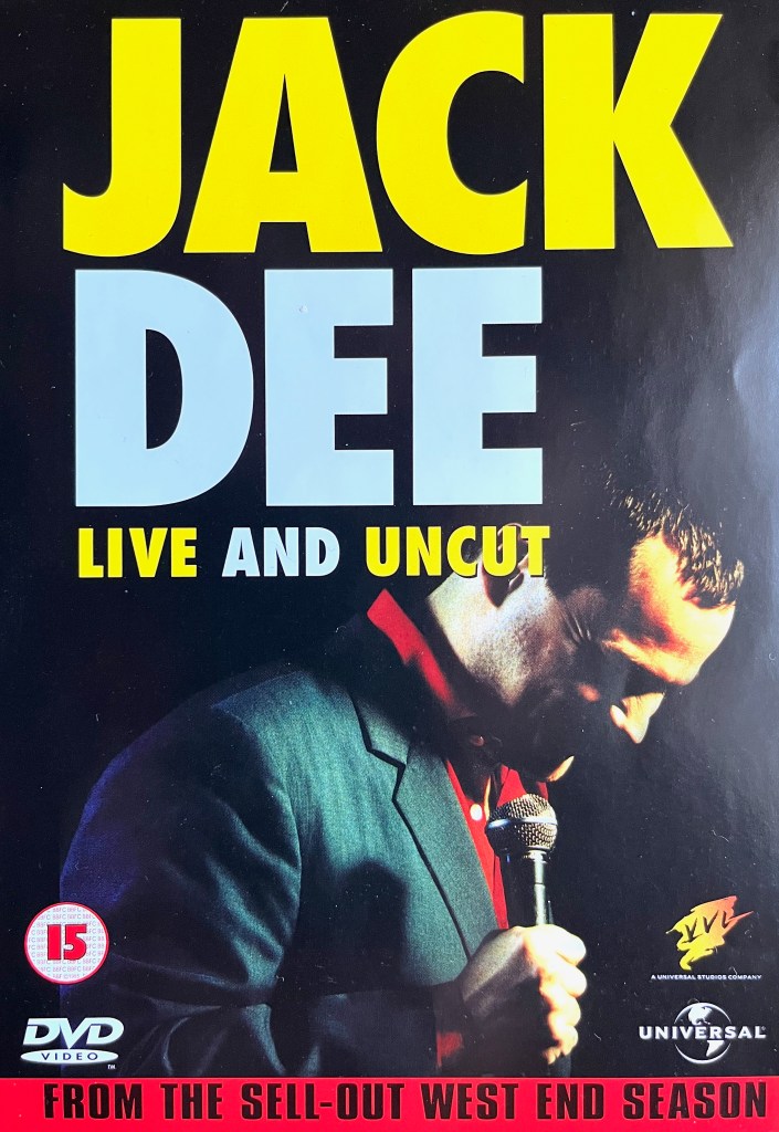 Front cover of the DVD for Jack Dee Live And Uncut. Against a black background, the title is in block capitals at the top, with the words in alternating colours of yellow and white, Jack Dee's name being larger than the show's title beneath it. In the bottom half of the cover, slightly overlapped by the title and lit by a spotlight, Jack is holding a microphone and has his head bowed slightly as he laughs.