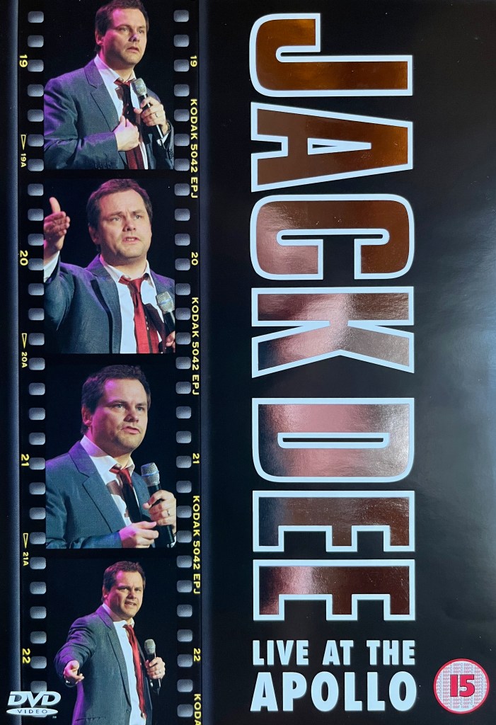 Front cover of the DVD for Jack Dee Live At The Apollo. Down the left side of the cover is a film strip showing 4 images of Jack Dee talking on stage as he holds a microphone, wearing a grey jacket, red tie and white shirt. HIs name, turned on its side, runs down the right side of the cover in large letters. The letters are slightly reflective and have a white border.