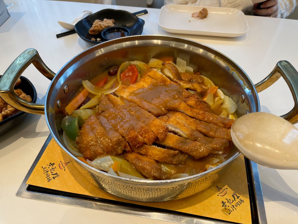Golden Chicken Katsu Hotpot, a large round metal pot with a handle on each side, filled with strips of chicken and assorted vegetables.