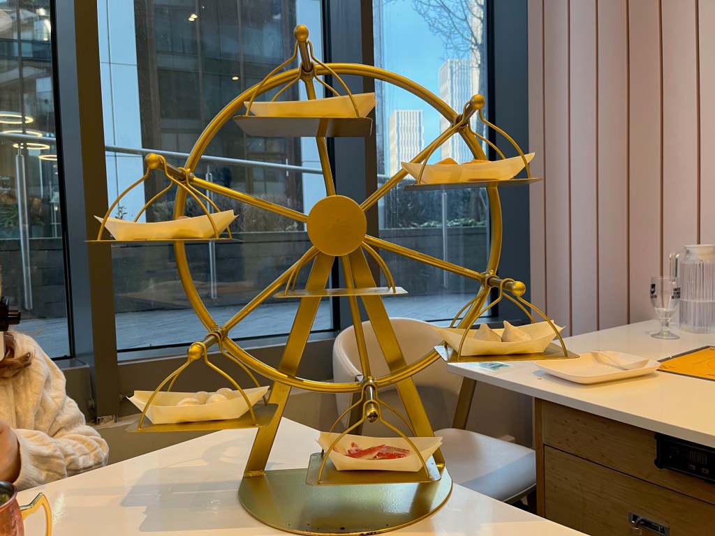 A large ferris wheel contraption on a restaurant table, holding small dishes of food on 6 platforms.