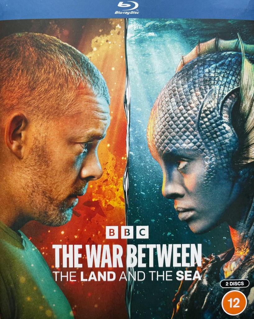 Front cover of the Blu-ray for The War Between The Land And The Sea. It shows an image split into two vertical halves. On the left is a headshot of Barclay, a man with extremely short hair so he looks almost bald, in front of a background of fiery explosions. On the right is a headshot of Salt, a female with blue skin and a scaly forehead, in front of an underwater background. The two of them face each other across the watery dividing line in the centre of the image with stern looks on their faces. Across the bottom of the image is the BBC logo and the show's title.