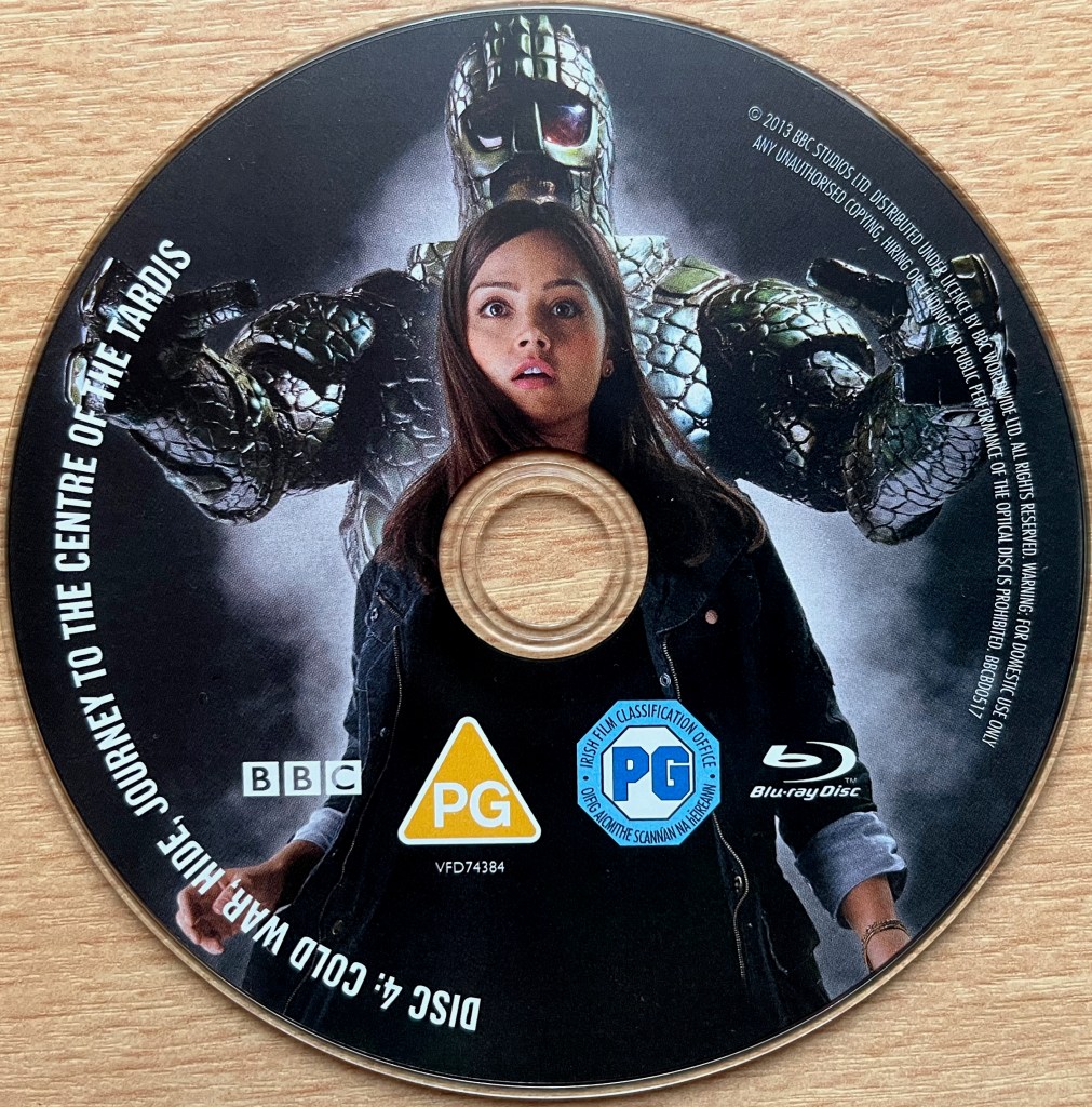 Disc 4 in the Doctor Who Series 7 Blu-ray set, showing an image of Clara with a large creature wearing a mask behind her. Around the edge of the disc are the episode names Cold War, Hide and Journey To The Centre Of The Tardis, along with copyright information.