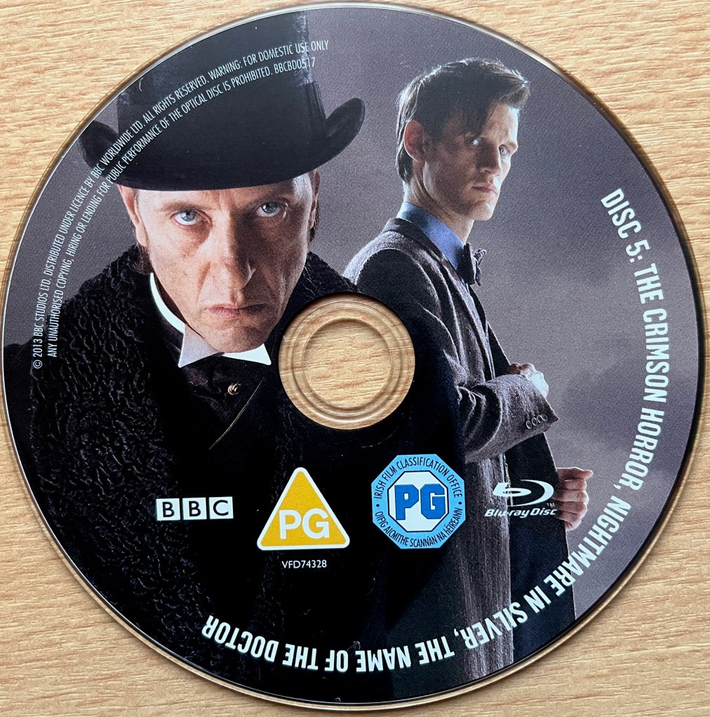 Disc 5 in the Doctor Who Series 7 Blu-ray set, showing an image of The Great Intelligence and Matt Smith's Doctor. Around the edge of the disc are the episode names The Crimson Horror, Nightmare In Silver and The Name Of The Doctor, along with copyright information.