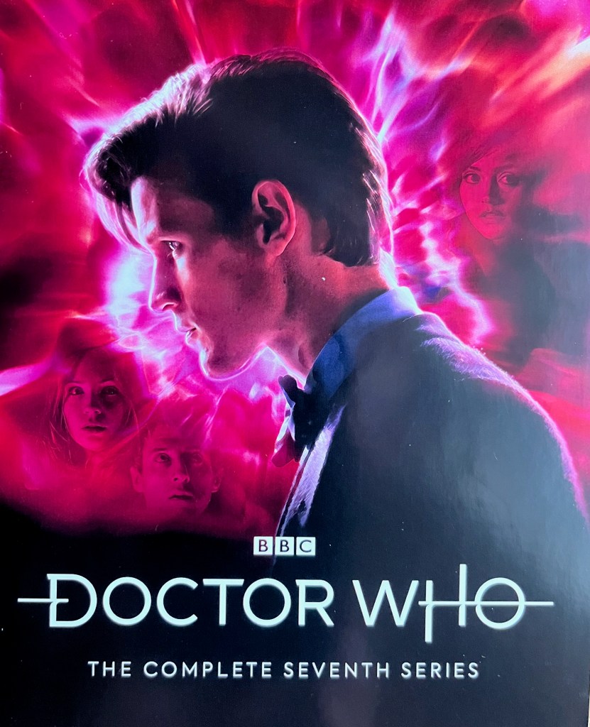 Front side of the leaflet included with the Doctor Who Series 7 Blu-ray Steelbook, featuring a photo of Matt Smith's Doctor in profile, in front of an exploding, swirling vortex with colours of red, pink purple and white vortex, in which Amy, Rory and Clara's faces can be seen blended into the colour scheme.