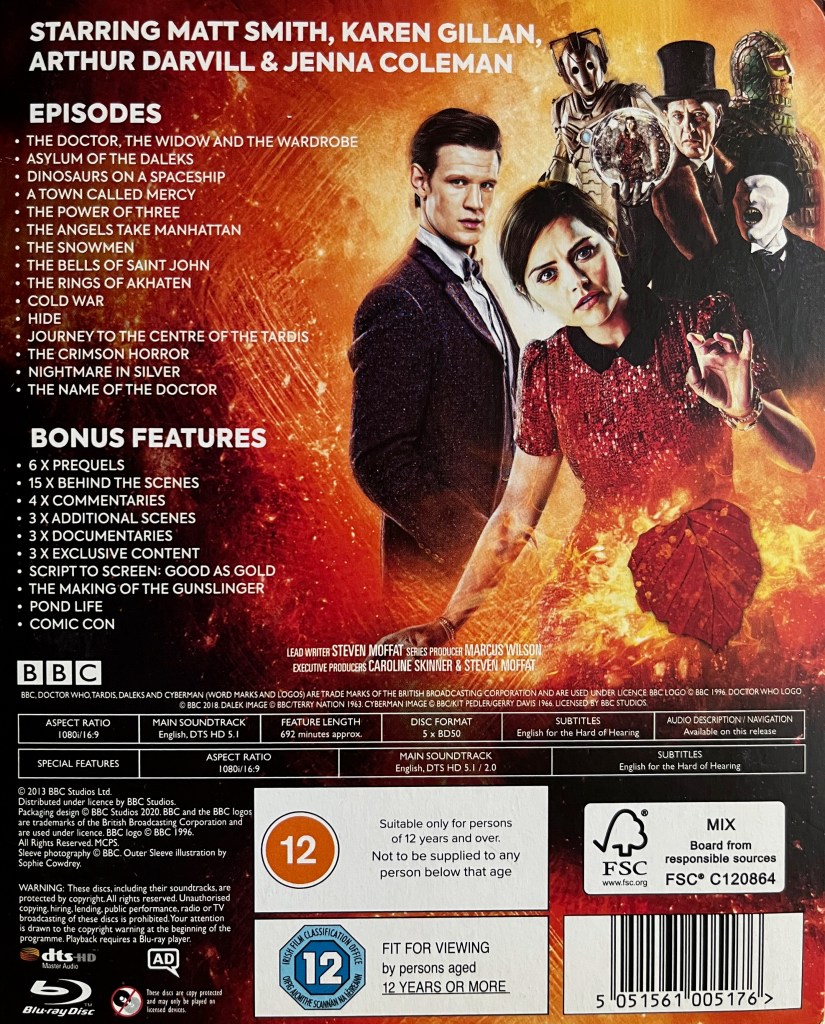 The back of the cardboard slipcase cover for the Doctor Who Series 7 Blu-ray steelbook. To the right of the list of episodes and extra features is an image showing Matt Smith's Doctor standing next to Clara, while behind them are the Tardis and various characters including The Great Intelligence and a Cyberman.