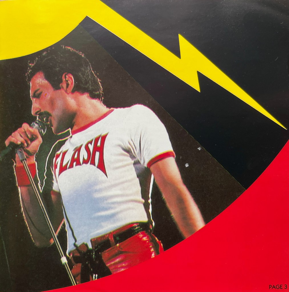 A photo of Freddie Mercury singing into a microphone, while wearing a white t-shirt   with the word Flash in large red letters on it. The photo is from the booklet with the Flash Gordon album, with a yellow streak of lightning above him.