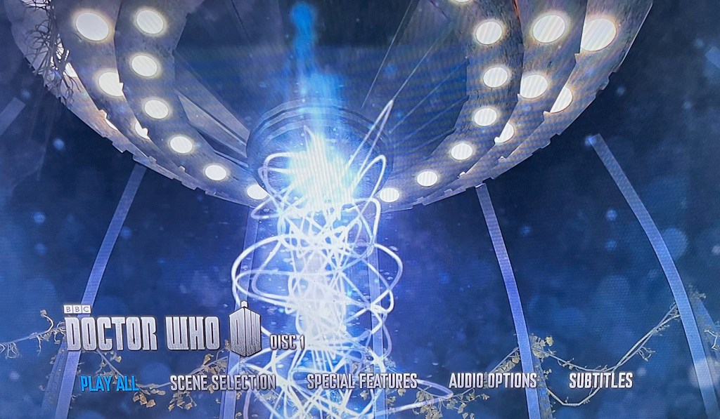 Main menu on the Blu-ray for Doctor Who Series 7. It shows the interior of the Tardis, with a close-up of a bright vertical tower of swirling light that's stretching down from the ceiling. At the bottom of the screen is the Doctor Who logo, along with options for Play All, Scene Selection, Special Features, Audio Options and Subtitles.