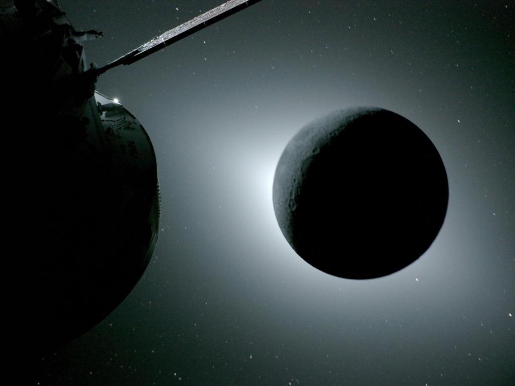A view from the Orion spacecraft of a solar eclipse, with the moon blocking out the sun, so that a hazy glow of light appears around the outside of it.