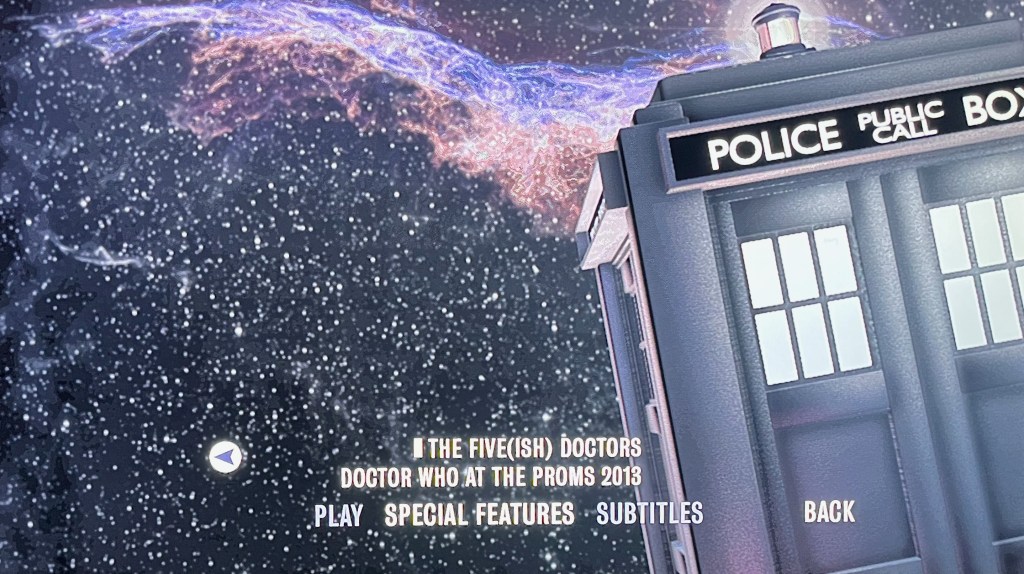 The final page of the special features menu on the Blu-ray for the Doctor Who biographical drama An Adventure In Space And Time, showing a close-up of the Tardis on the right, next to a large flurry of snow falling from the sky on the left. At the bottom are options to watch The Five(Ish) Doctors and Doctor Who At The Proms 2013.