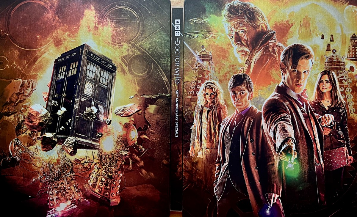 The cover spread artwork for the Doctor Who 50th Anniversary Specials Blu-ray steelbook. The front cover, on the right, shows Matt Smith, David Tennant and John Hurt as their respective iterations of the Doctor, along with companions Clara Oswald and Rose Tyler, while Daleks and their spaceships swarm around in an explosive, fiery background, in amongst which is the large dome on the planet Gallifrey. The back cover on the left shows a battered Tardis flying in front of a huge fireball, with Daleks exploding around it.