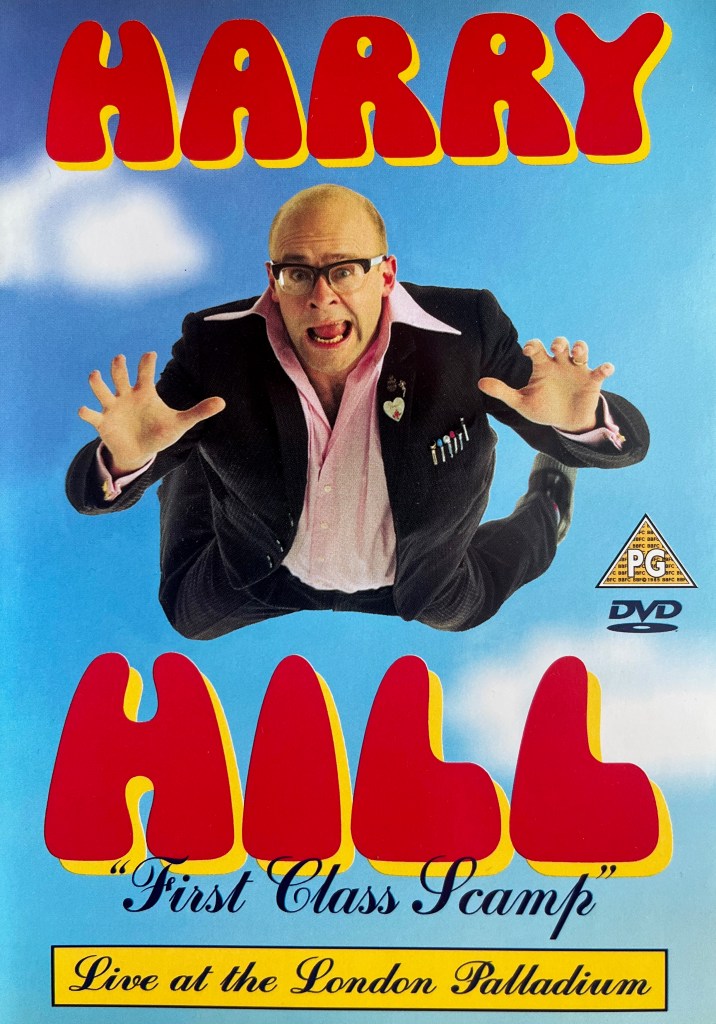 Front cover for Harry Hill's First Class Scamp DVD, showing a view of him falling through the sky towards us. The word Harry is above him, and Hill beneath him, each in large red letters with a yellow shadow.