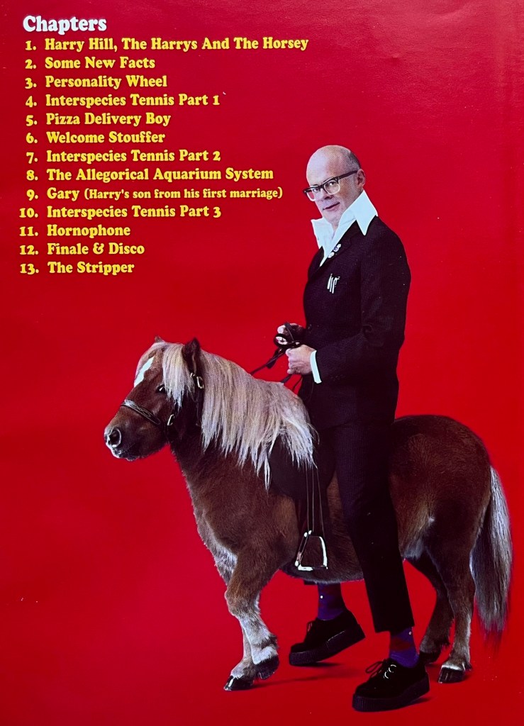 Inside of the cover sleeve for Harry Hill's Hooves DVD. Against a red background is a list of chapters on the DVD in yellow text, and to the write of that is an image of Harry on a small horse, viewed from the side as he looks across at us. Chapter headings include Harry Hill, The Harrys And The Horsey, Personality Wheel, Interspecies Tennis, Welcome Stouffer, the Allegorical Aquarium System, Gary, Hornophone and The Stripper.