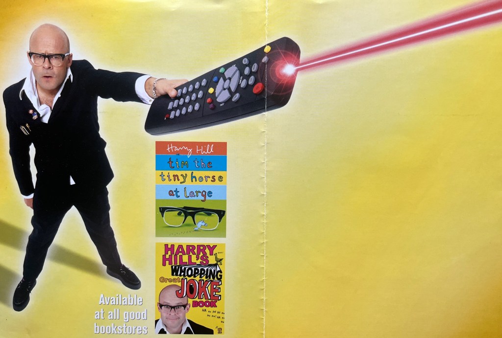 The inside spread of the DVD cover for Harry Hill's TV Burp Gold. It shows Harry standing on the left hand side, pointing a large remote control and pressing a button so that a laser-like ray fires out of it into the top-right corner of the right page.