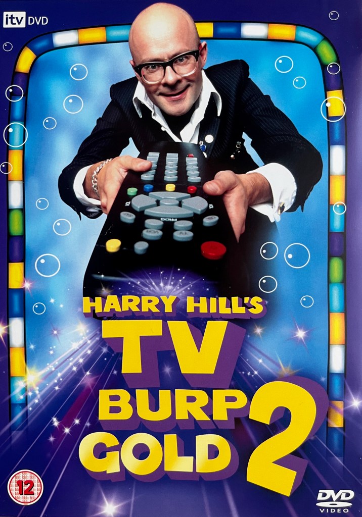 Front cover of the DVD for Harry Hill's TV Burp Gold 2. It shows Harry standing in front of a screen as he points a large remote control towards us, while the title is shown in large yellow letters at the bottom of the cover.