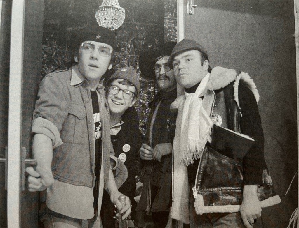 Black and white photo of the gang from Citizen Smith, with Wolfie, Ken, Tucker and Speed looking a bit concerned as they look towards something in the distance off camera to the left.
