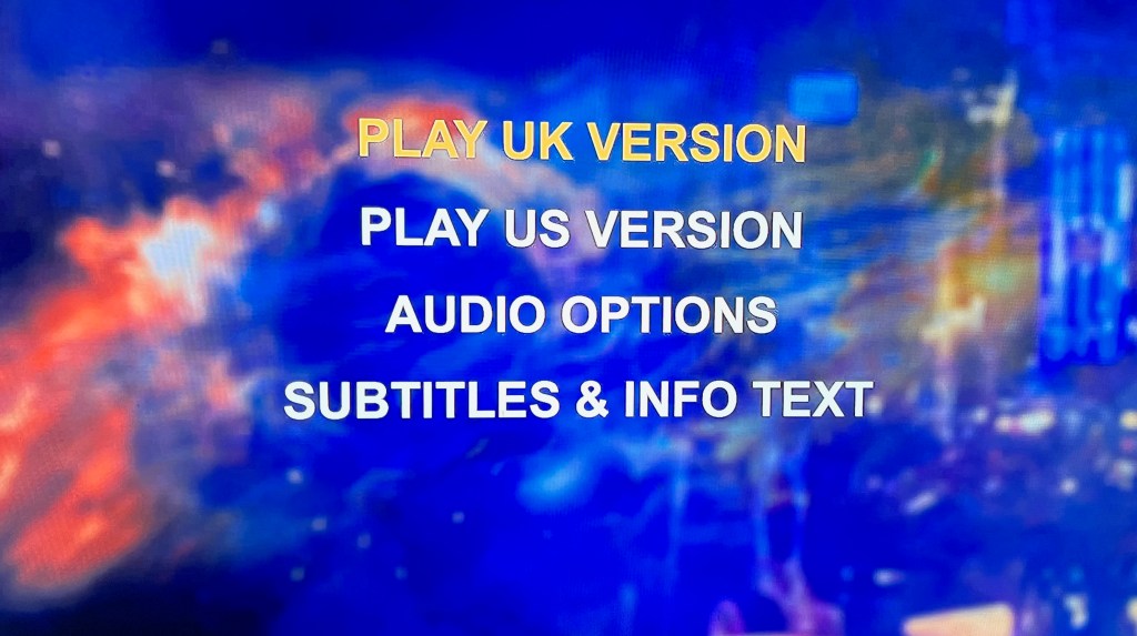 Audio navigation menu on the Blu-ray for the Doctor Who movie, with 4 options in large, bold, white capital letters against a blurred image of the blue-coloured universe in the background, so the options stand out really clearly. The options are Play UK Version, Play US Version, Audio Options, and Subtitles and Info Text.