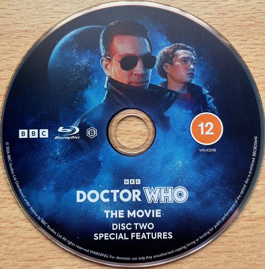 Blu-ray disc 2 for Doctor Who the movie, containing the special features. It shows the Master with companion Chang Lee, while a planet floats in space in the background.