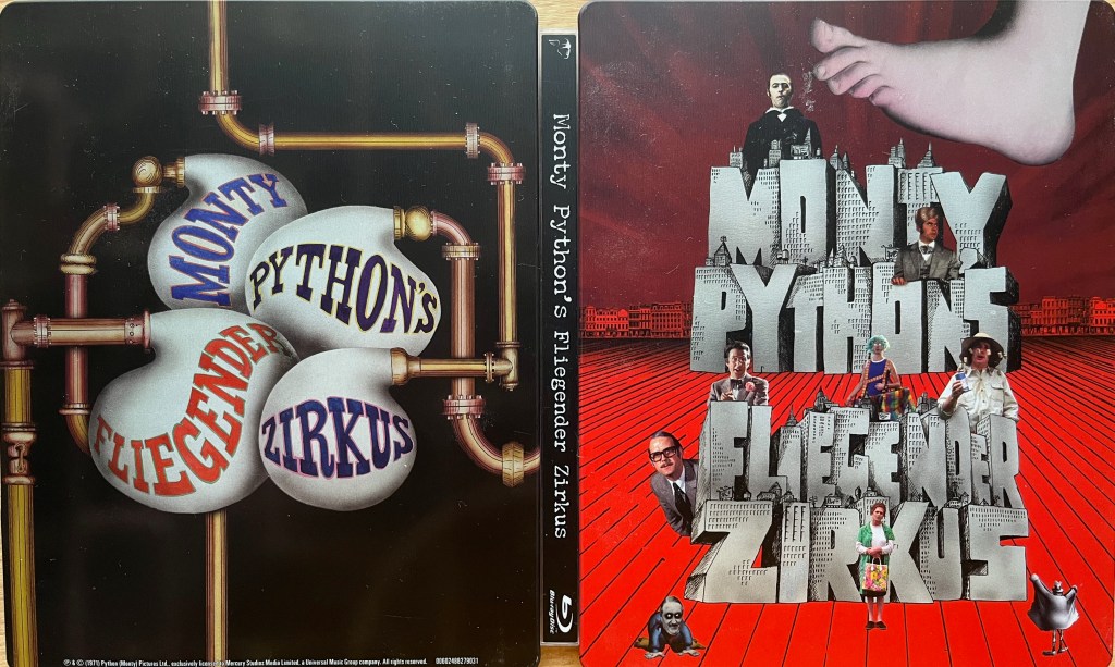 The exterior of the Blu-ray steelbook for Monty Python’s Fliegender Zirkus. The front cover on the right shows the title in large stone letters, one word per line, each letter having tiny buildings on top of it. The various members of Monty Python are spread around the cover wearing a variety of outfits. A large foot is about to stamp on the structure from the top right. The back cover on the left, meanwhile, has a network of pipes, with 4 of them blowing large bubbles that meet in the centre, each bubble containing one word of the title.
