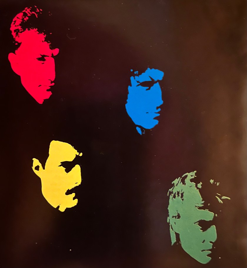 An artistic image showing images of the 4 members of Queen against a black background. Each is facing forward with light hitting their face from the left side of the image, leaving the other side of each face in shadow, blending into the black behind them. Each face is shown in a different colour, with John in red, Brian in blue, Freddie in yellow and Roger in green.
