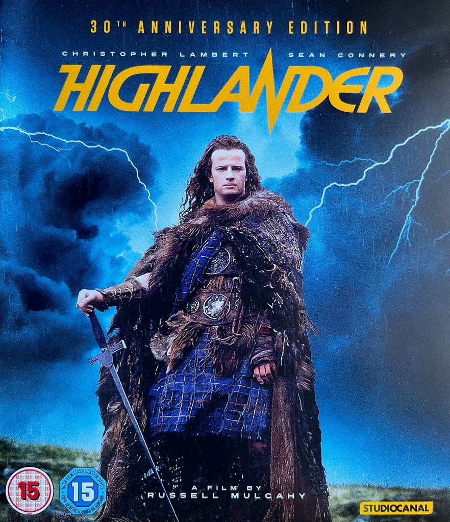 Front cover for the Blu-ray of Highlander, showing lead character Connor MacLeod wearing a large fur coat over a blue tartan outfit, standing in front of a dark stormy sky with streaks of lightning.
