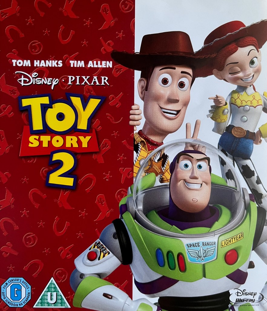 Blu-ray front cover for Toy Story 2. On the left, the logo of the film is shown over a dark red background embossed with symbols including horseshoes, stars, cowboy boots and the letter J in a circle. On the right, cowboy Woody, cowgirl Jessie and Space Ranger Buzz are posing together.