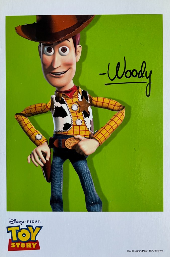 A Toy Story art card showing cowboy Woody standing against a green background, with his signature in black next to him.