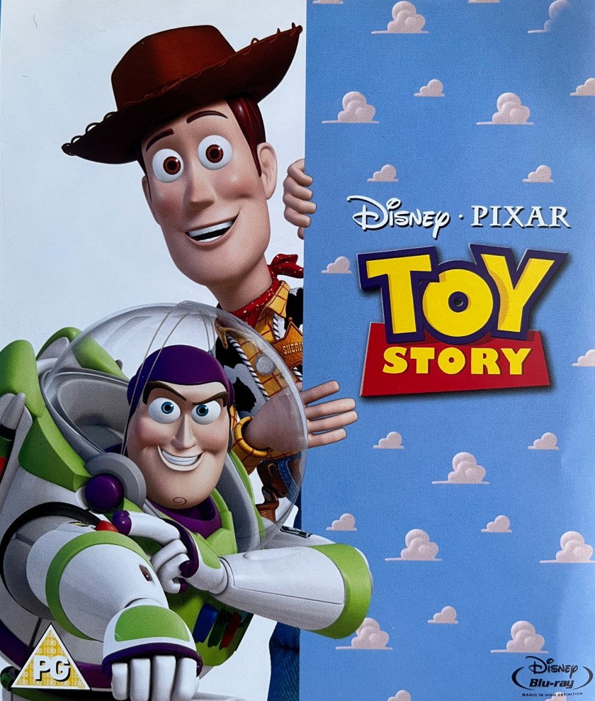 Blu-ray front cover for the first Toy Story film. On the right, the logo for the film is on a blue wall covered in little white clouds. On the left, cowboy Woody is peering around the side of that wall, while Space Ranger Buzz is firing the laser on the arm of his spacesuit.
